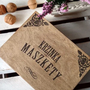 Drewniana skrzynka z napisem Krzinka na Maszkety na białym stole.