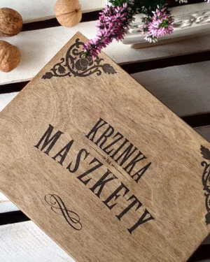 Drewniana skrzynka z napisem Krzinka na Maszkety na białym stole.