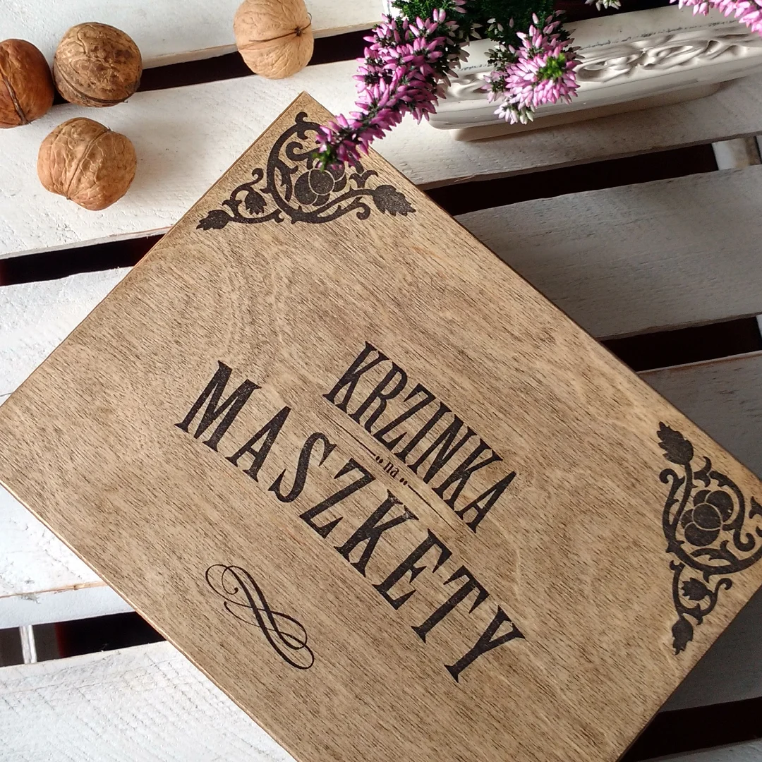 Drewniana skrzynka z napisem Krzinka na Maszkety na białym stole.