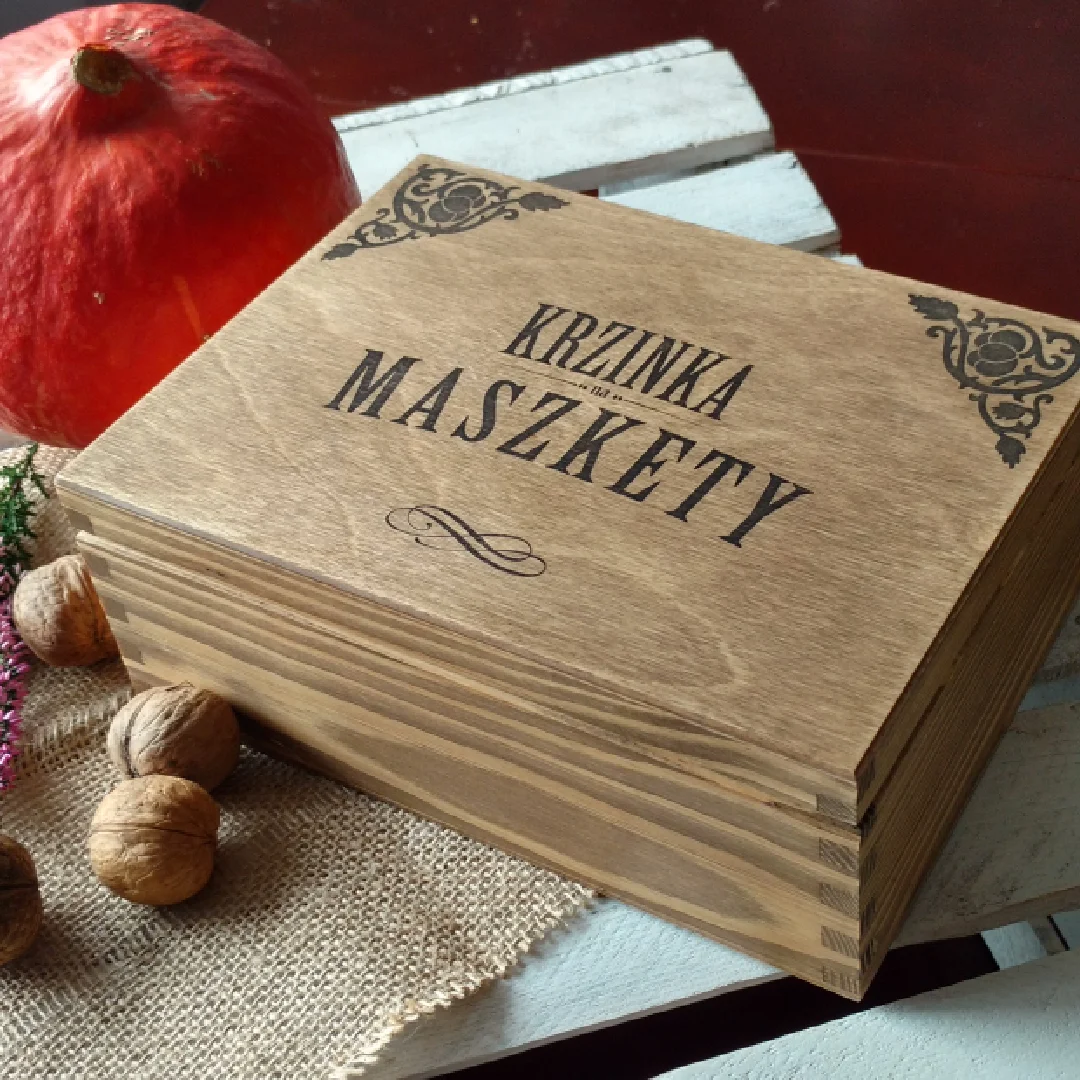 Drewniana skrzynka z napisem Krzinka na maszkerty, obok dynia i orzechy.