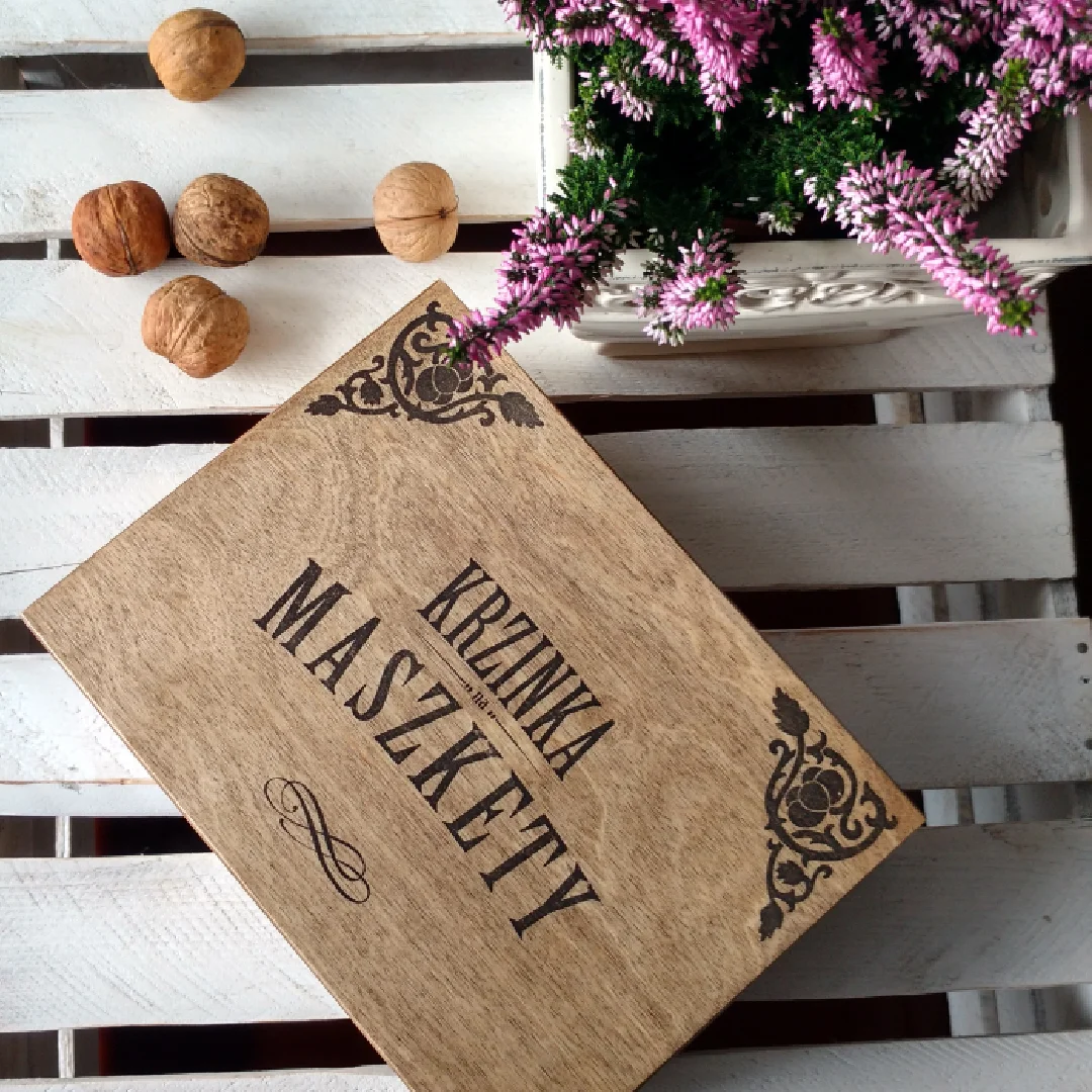 Drewniana skrzynka z napisem Krzinka na maszkerty na białym stole.