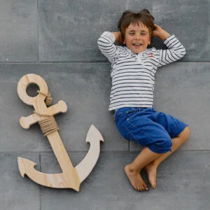 Chłopiec leży obok drewnianej kotwicy na szarej podłodze.