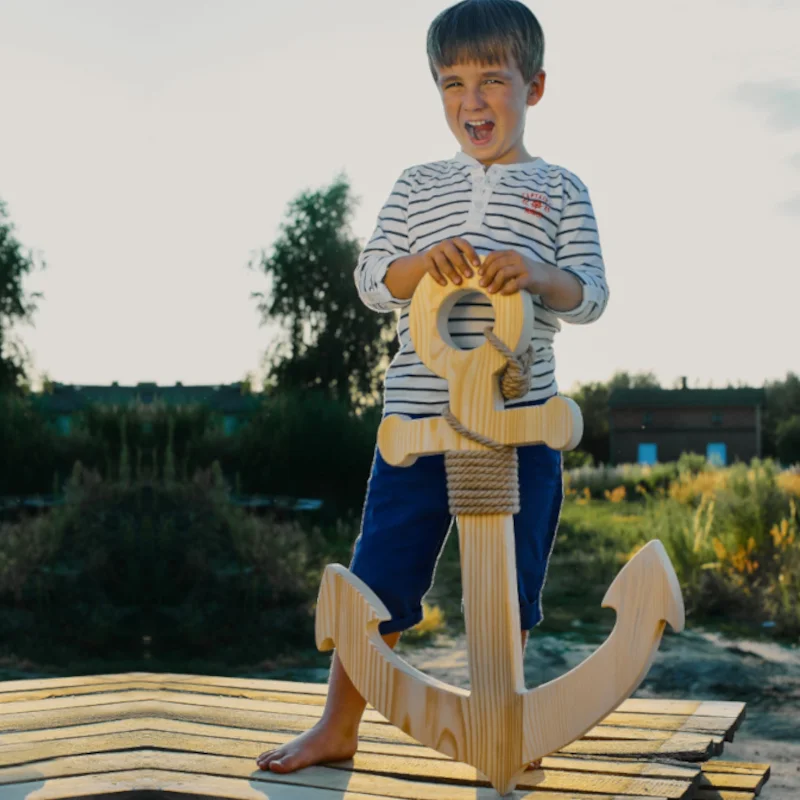 Chłopiec z drewnianą kotwicą na tle natury