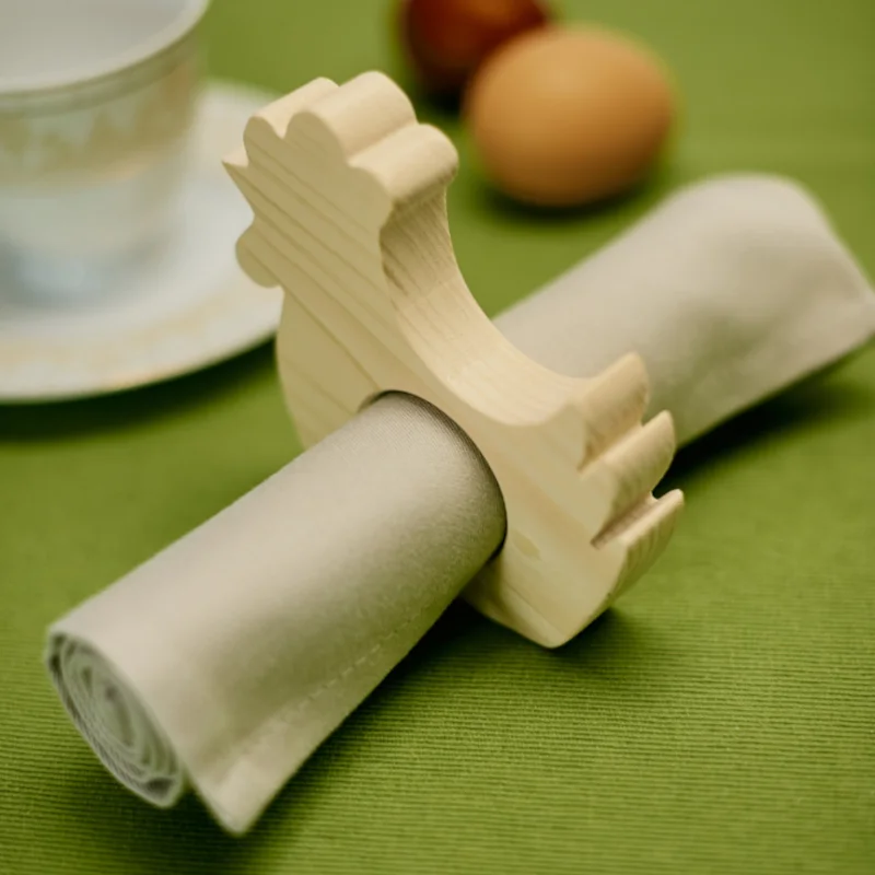 Drewniany uchwyt na serwetkę w kształcie koguta na zielonym obrusie.