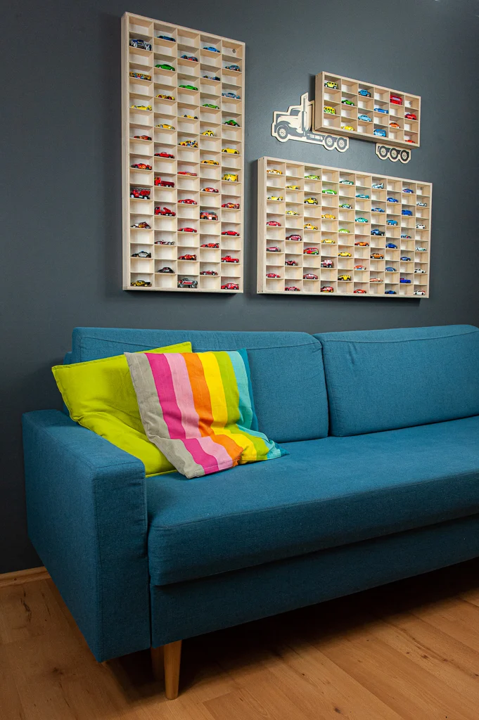Niebieska sofa z kolorowymi poduszkami, półki z modelami aut na ścianie.