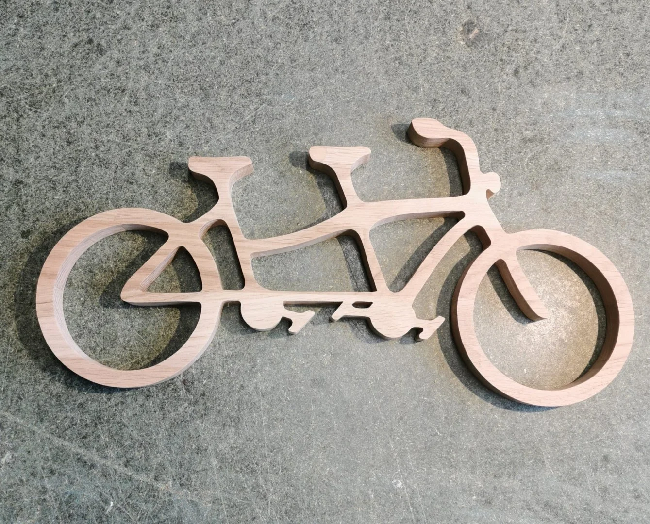 Drewniana dekoracja w kształcie roweru tandemowego na szarej powierzchni.