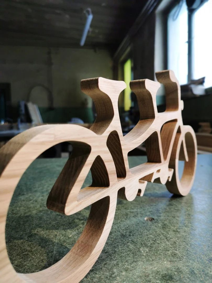 Drewniany model roweru tandem na stole warsztatowym.