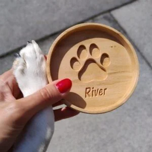 Drewniana podkładka z wyciętym śladem łapy i napisem 'River'.