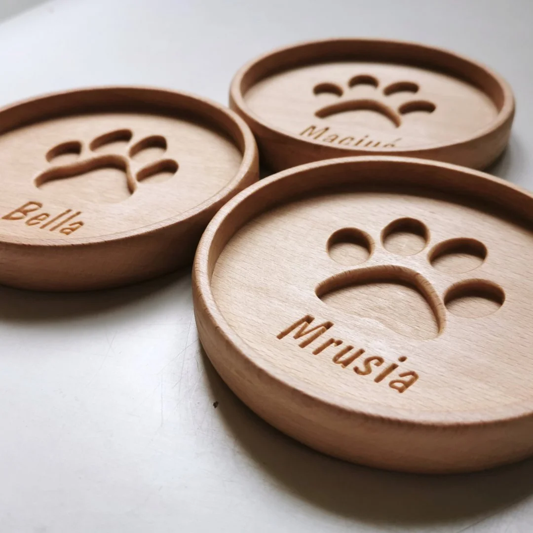 Trzy drewniane podkładki z wyciętymi łapkami i imionami.