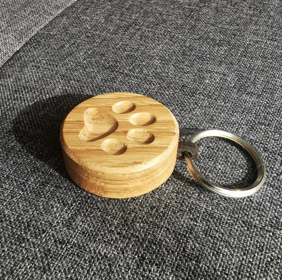 Drewniany breloczek z odciskiem łapki na szarym tle.
