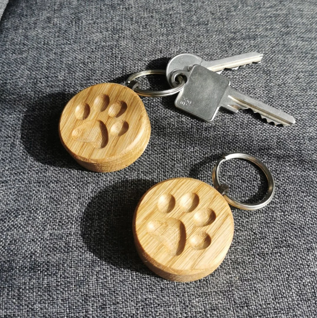 Dwa drewniane breloczki z odciskiem łapki na szarym tle.