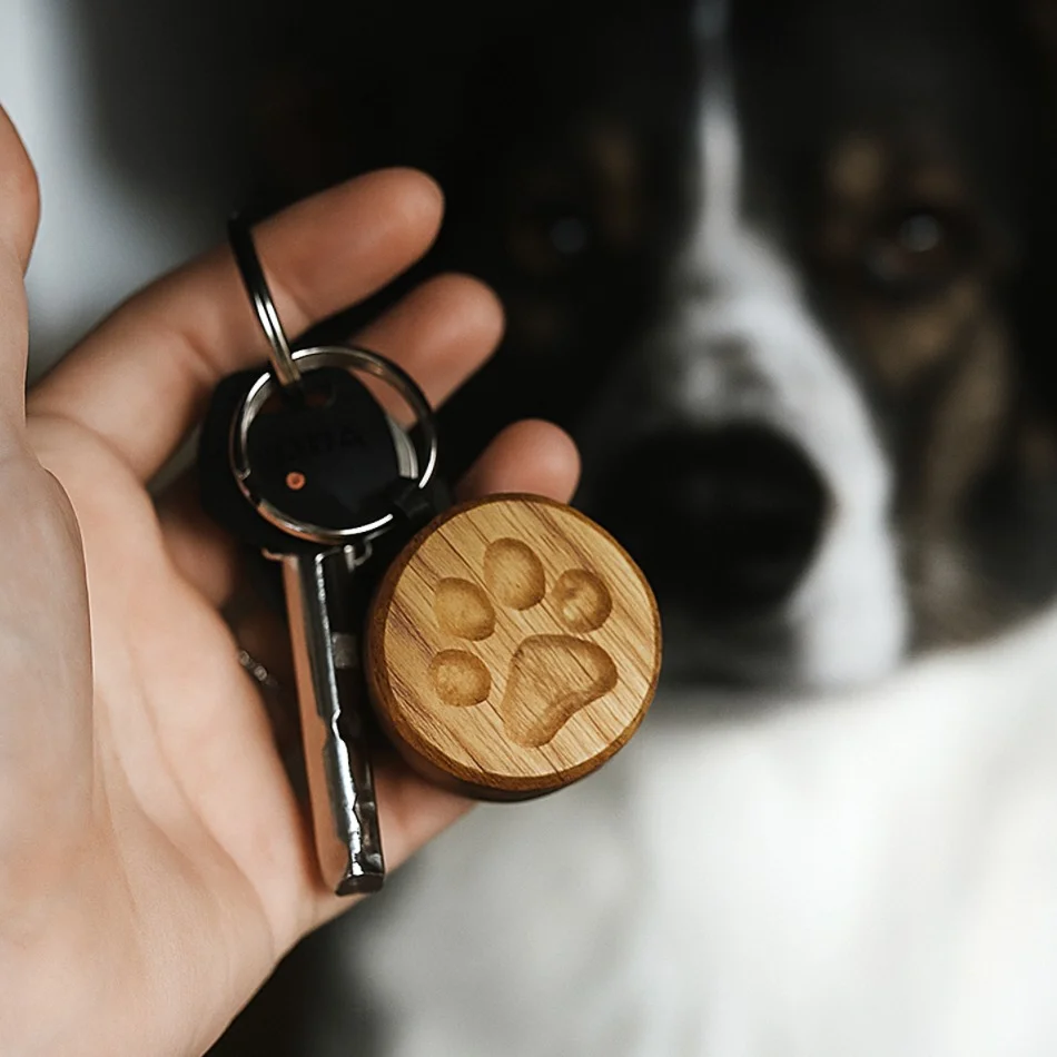 Drewniany breloczek z odciskiem łapki psa lub kota trzymany w dłoni.