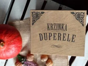 Drewniane pudełko z napisem 'Krzinka na duperele' obok dyni i orzechów.