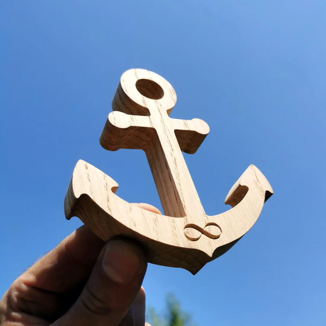 Drewniana kotwica trzymana w dłoni na tle nieba.