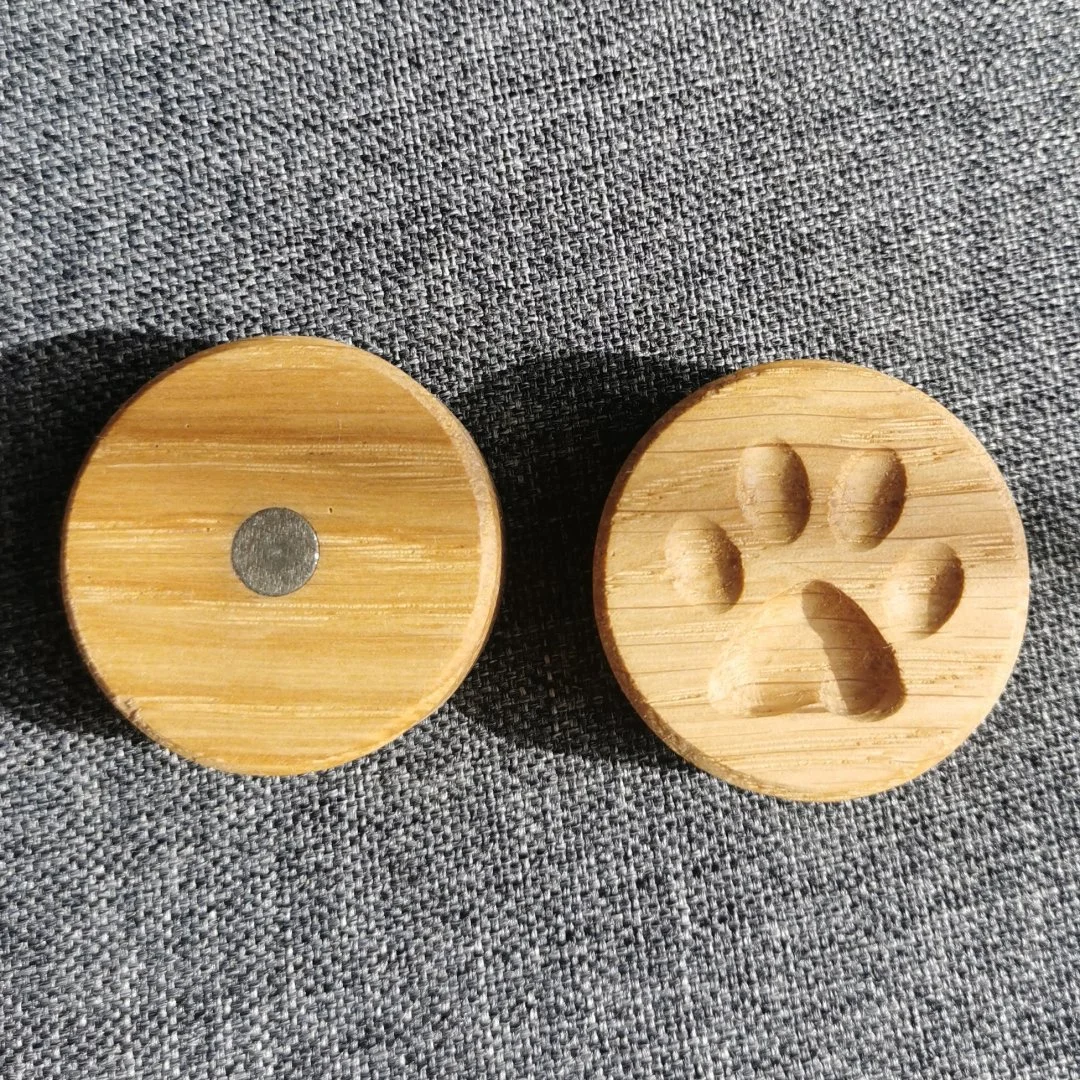 Drewniany magnes z wyżłobioną psia łapą na szarej tkaninie.