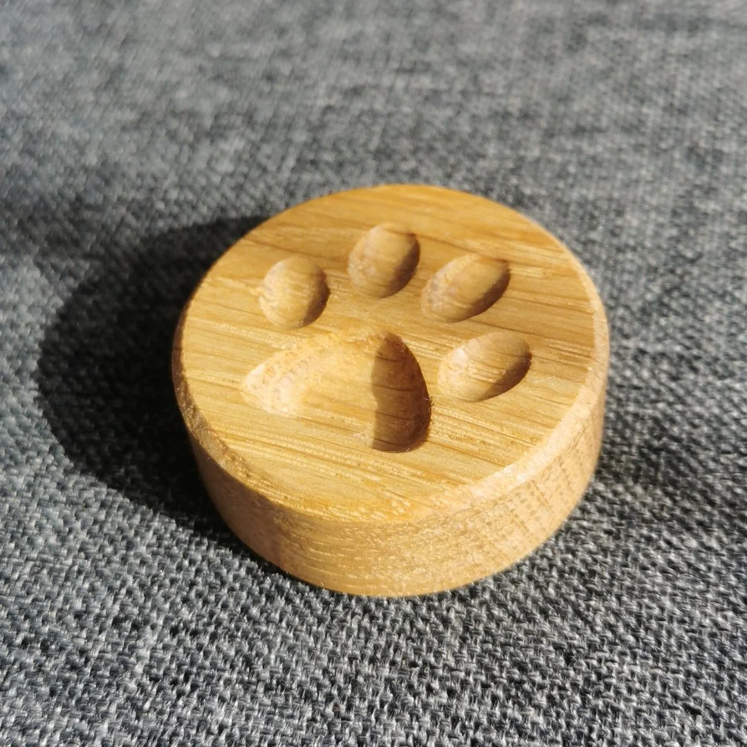 Drewniany magnes z wyżłobioną psia łapą na szarej tkaninie.