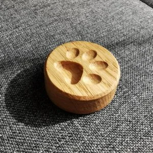 Drewniany magnes z wyżłobioną psia łapą na szarej tkaninie.