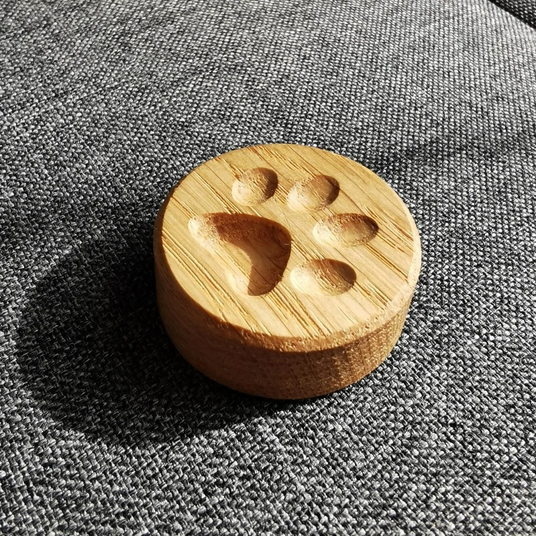 Drewniany magnes z wyżłobioną psia łapą na szarej tkaninie.