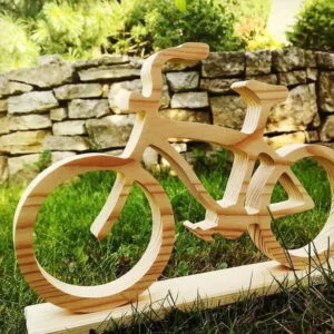 Mały drewniany rower na trawie przed kamiennym murem.