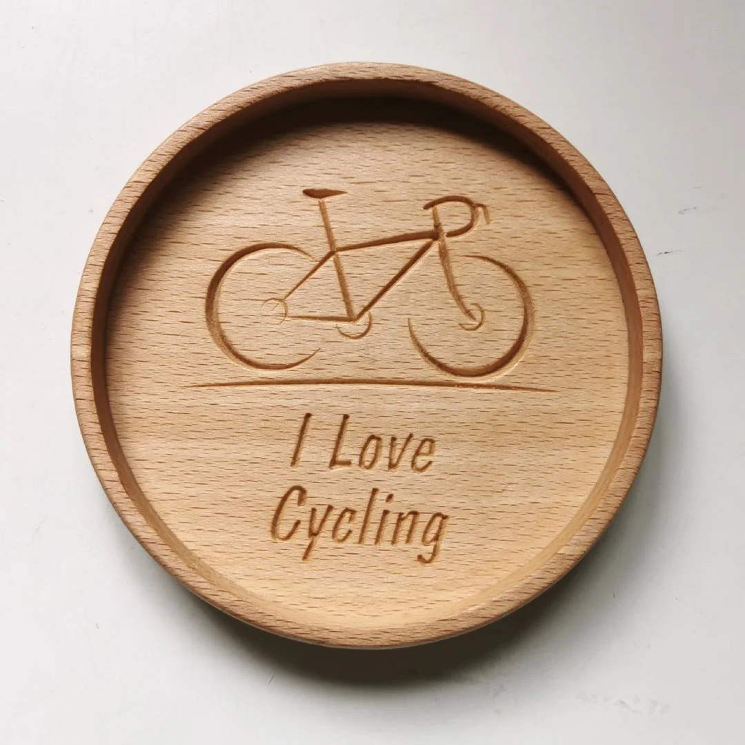 Drewniana podstawka z wygrawerowanym rowerem i napisem 'I Love Cycling'.
