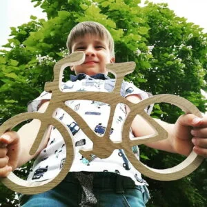 Chłopiec trzyma drewniany rower na tle drzewa.