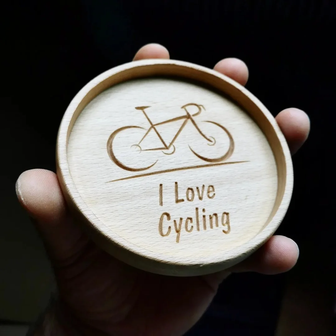 Drewniana podstawka z wygrawerowanym rowerem i napisem 'I Love Cycling'.