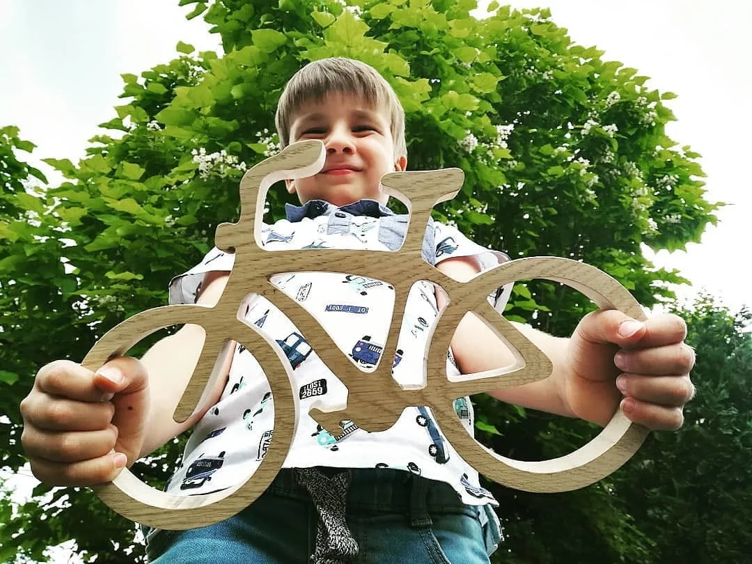 Chłopiec trzyma drewniany rower na tle drzewa.