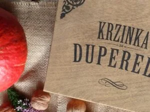 Drewniana skrzynka z napisem 'Krzinka na duperele' obok dyni i orzechów.