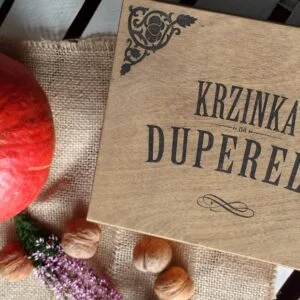 Drewniana skrzynka z napisem 'Krzinka na duperele' obok dyni i orzechów.
