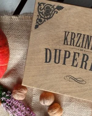 Drewniana skrzynka z napisem 'Krzinka na duperele' obok dyni i orzechów.