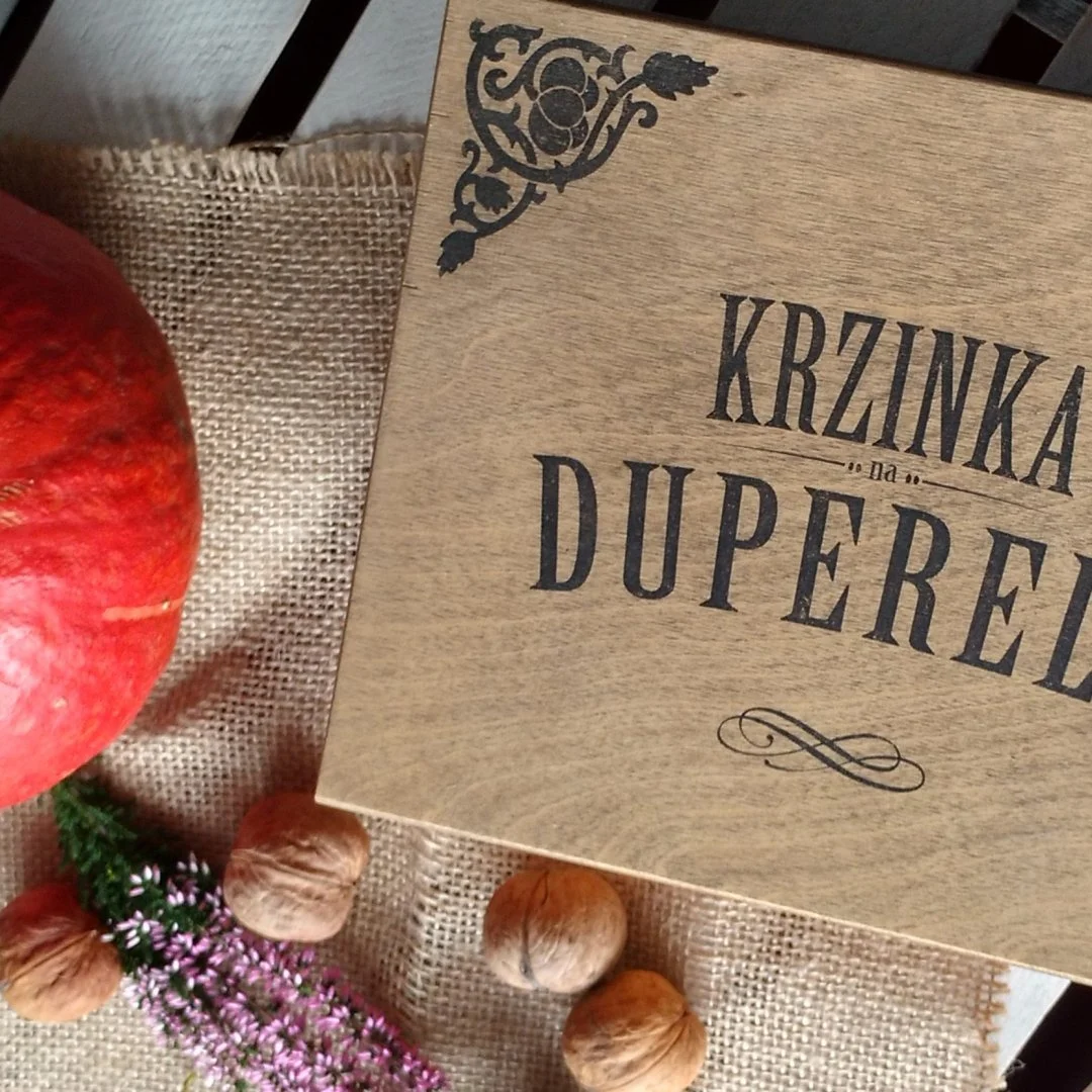 Drewniana skrzynka z napisem 'Krzinka na duperele' obok dyni i orzechów.
